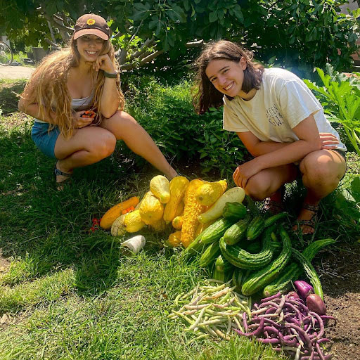 Two students kneeling beside large amounts of vegetables from the Sustainable GW Garden