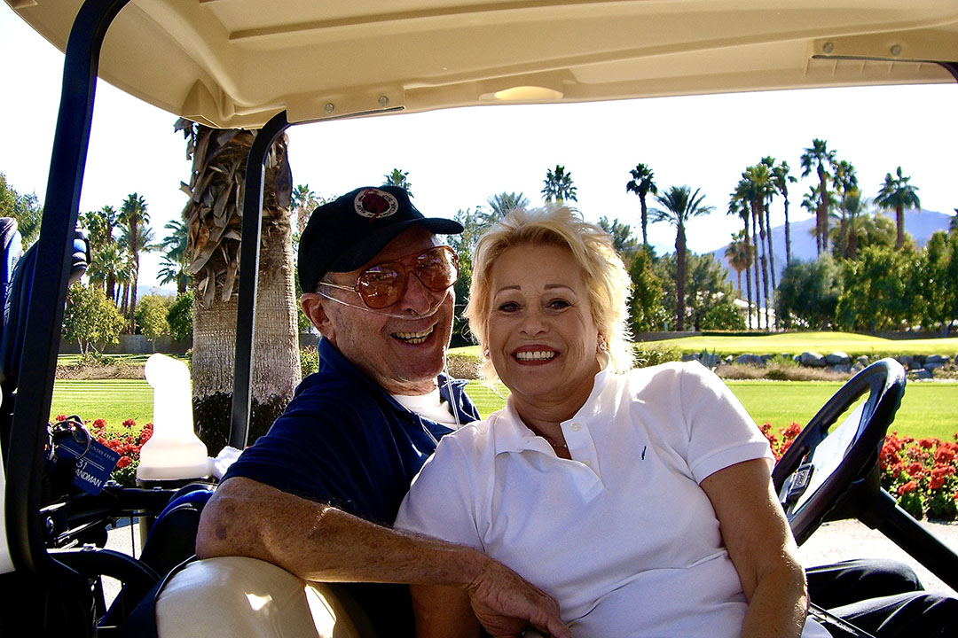 Saul and Joyce Brandman in a golf cart on a golf course on a sunny day. (Photo courtesy of Michelle Rubin)