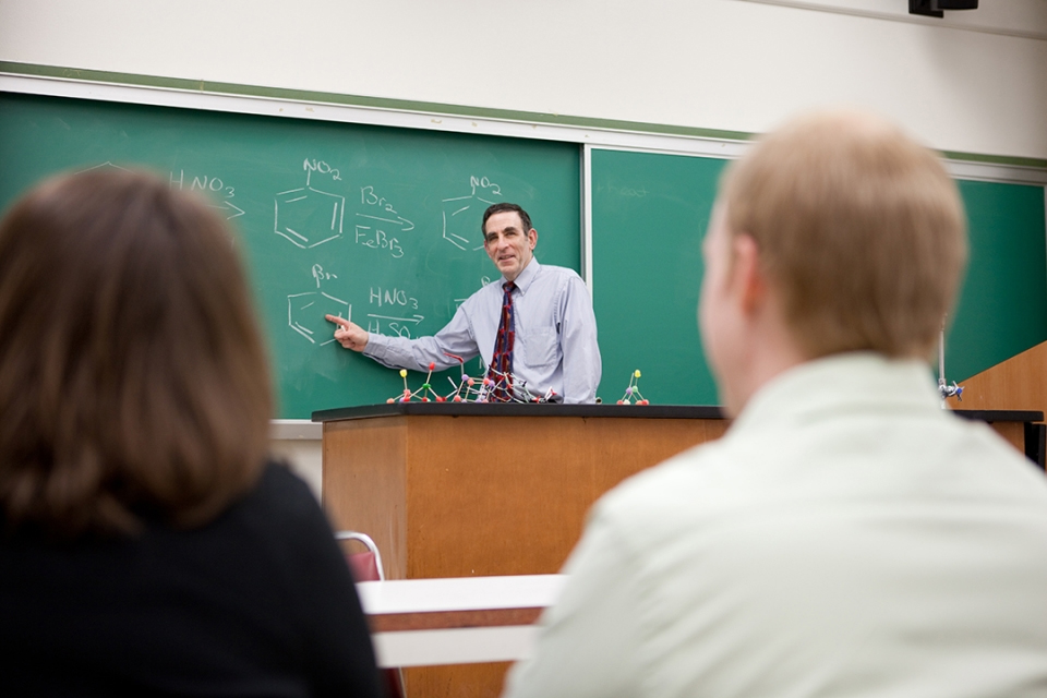 Professor Michael King shown at a blackboard demonstrating organic chemistry to a class.