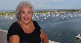 Dina Biblin on a balcony with a backdrop of a harbor with sailboats.